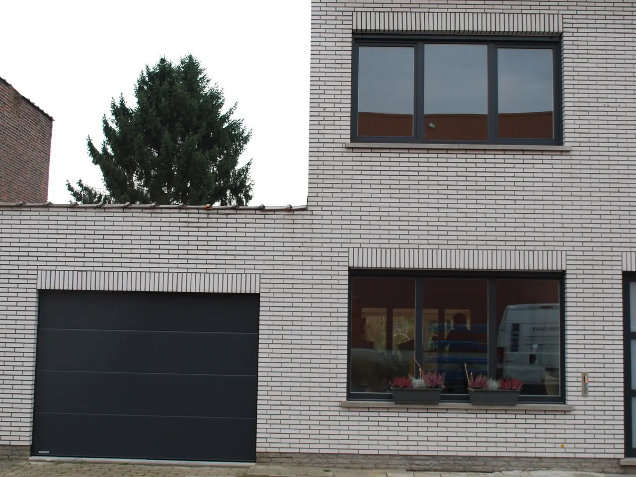 Antraciet sectionale garagepoort en ramen in een witte bakstenen gevel