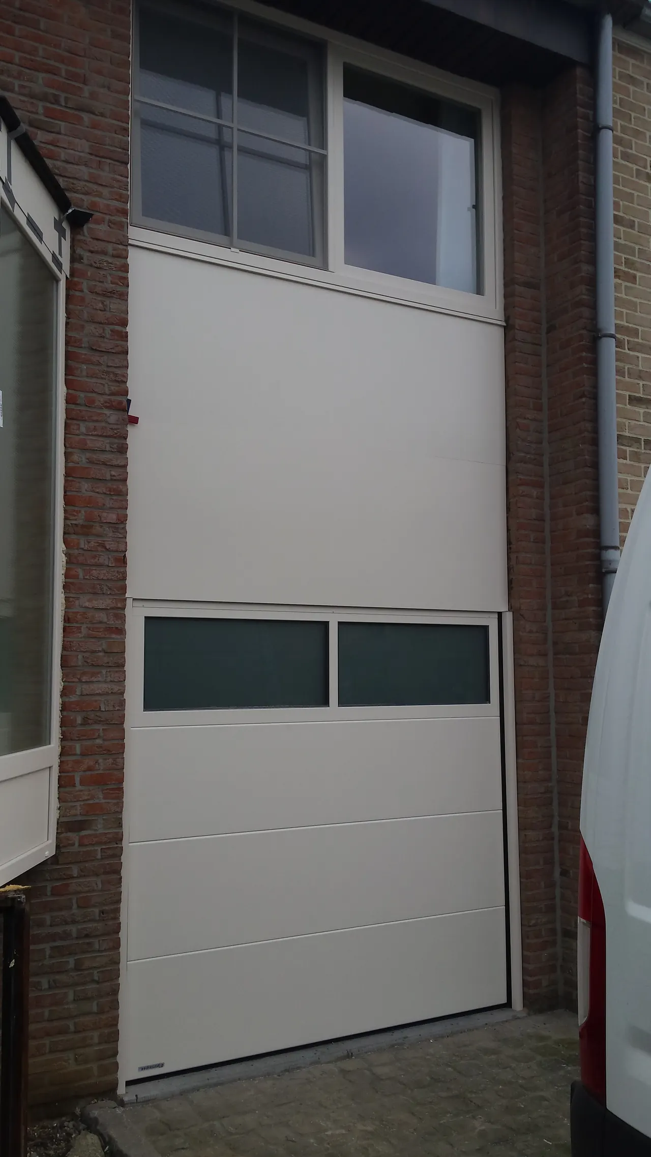 Witte sectionale garagepoort met glasstrook onder een raam