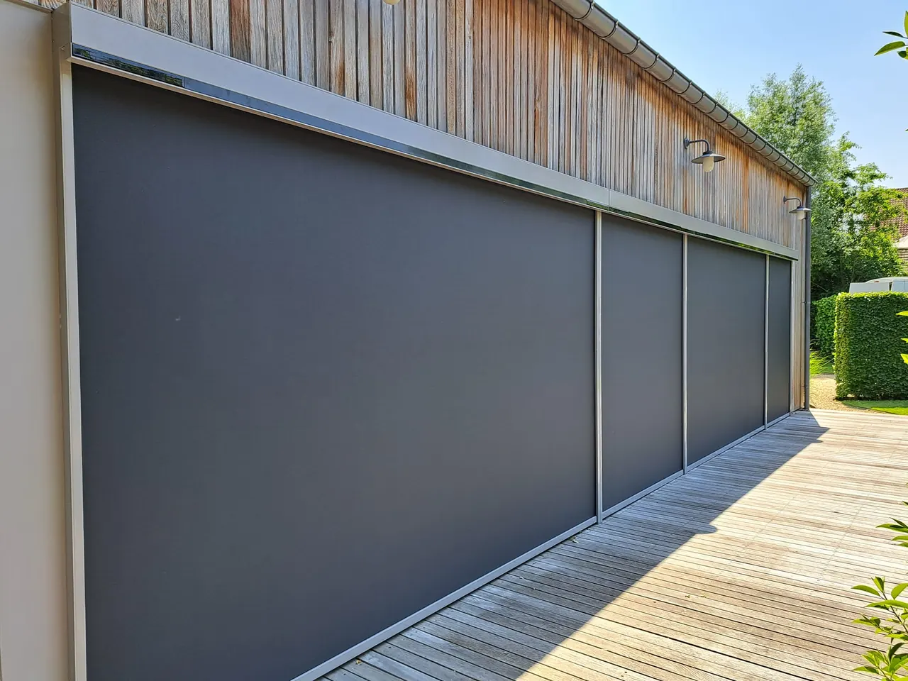 Rij antraciet screens over de volle lengte van een houten gevel met terras