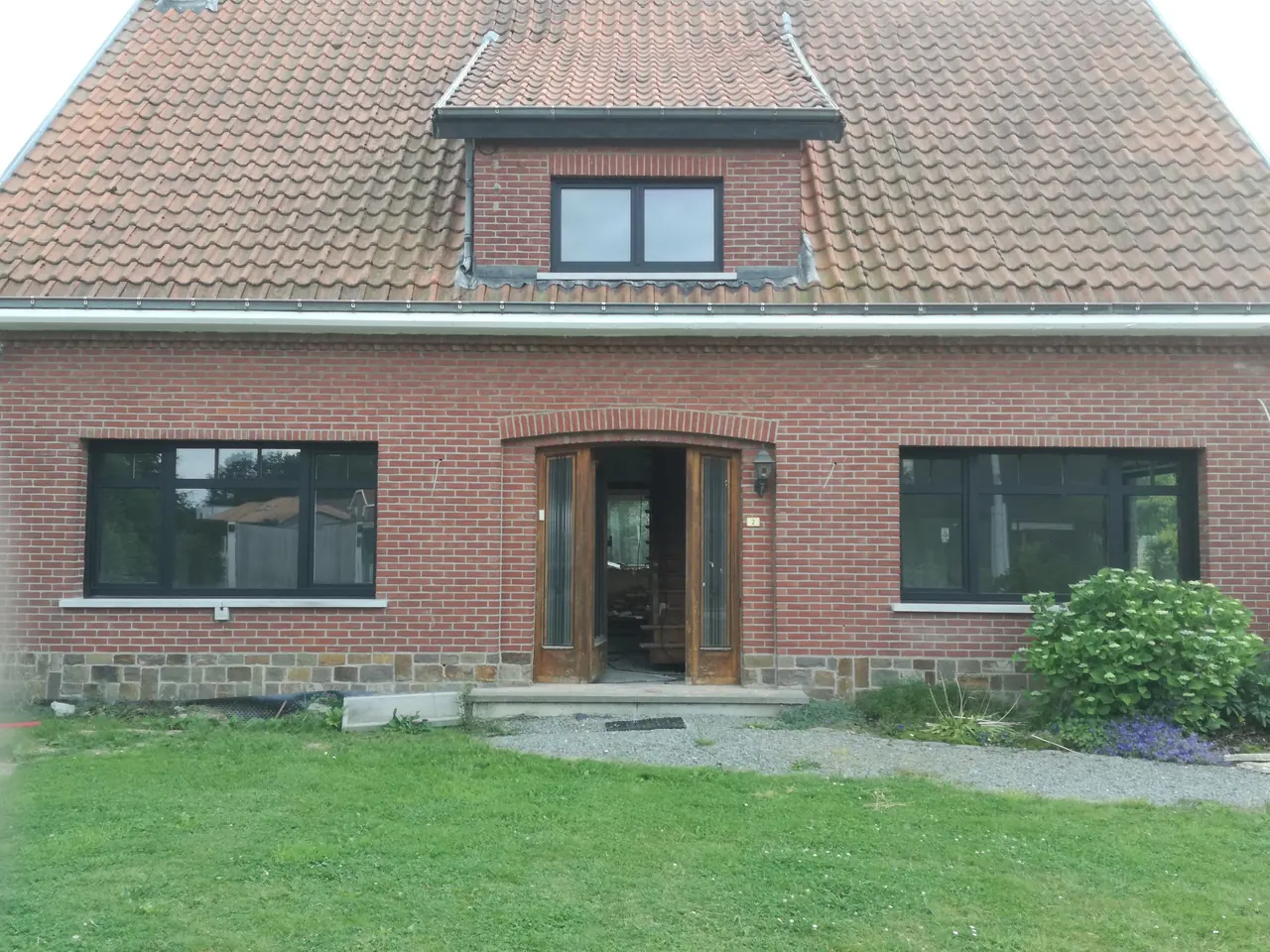 Bakstenen woning met nieuwe antraciet ramen rondom een houten voordeur